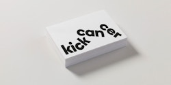 Pile of business cards designed for KickCancer on a table